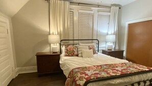 Une chambre à coucher avec un lit, des tables de chevet, une fenêtre avec des rideaux et une porte en bois.