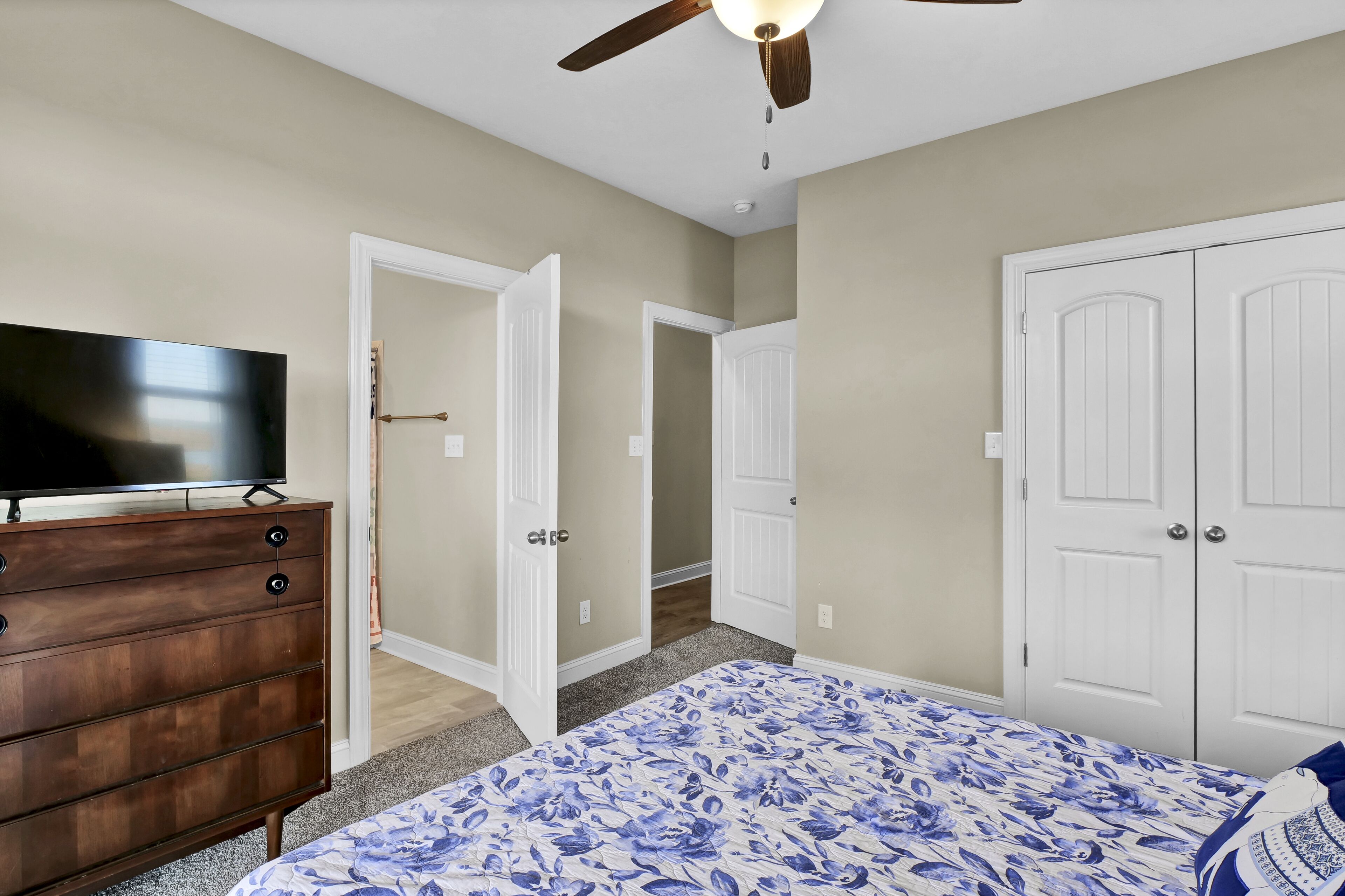 Une chambre à coucher avec un lit, une commode, un téléviseur et des portes blanches.