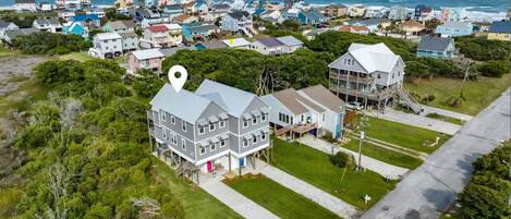 A coastal residential area with houses, a prominent house with a white marker, and a view of the ocean.