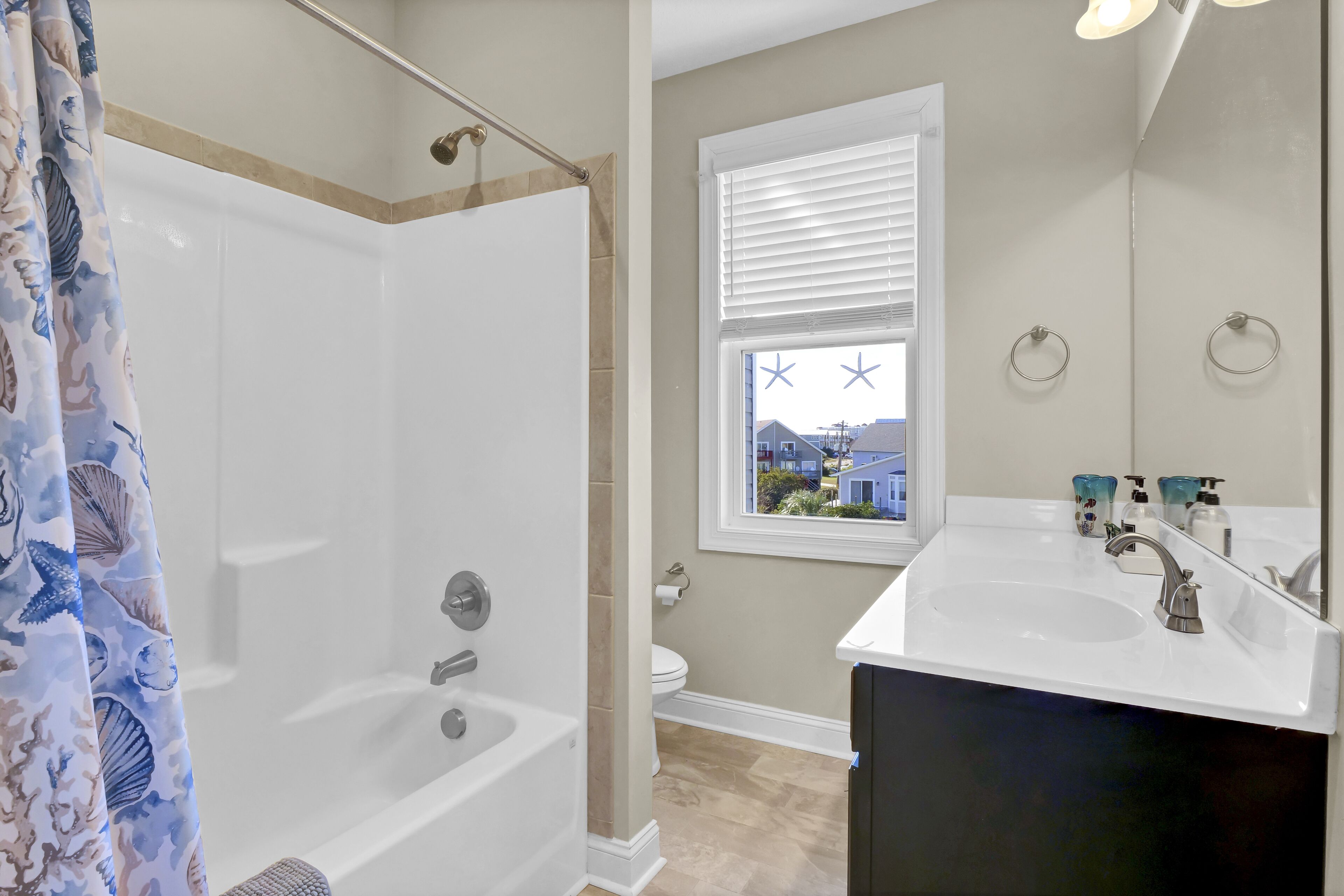 Une salle de bain avec une baignoire, des toilettes, une fenêtre avec des stores et un lavabo avec un miroir.
