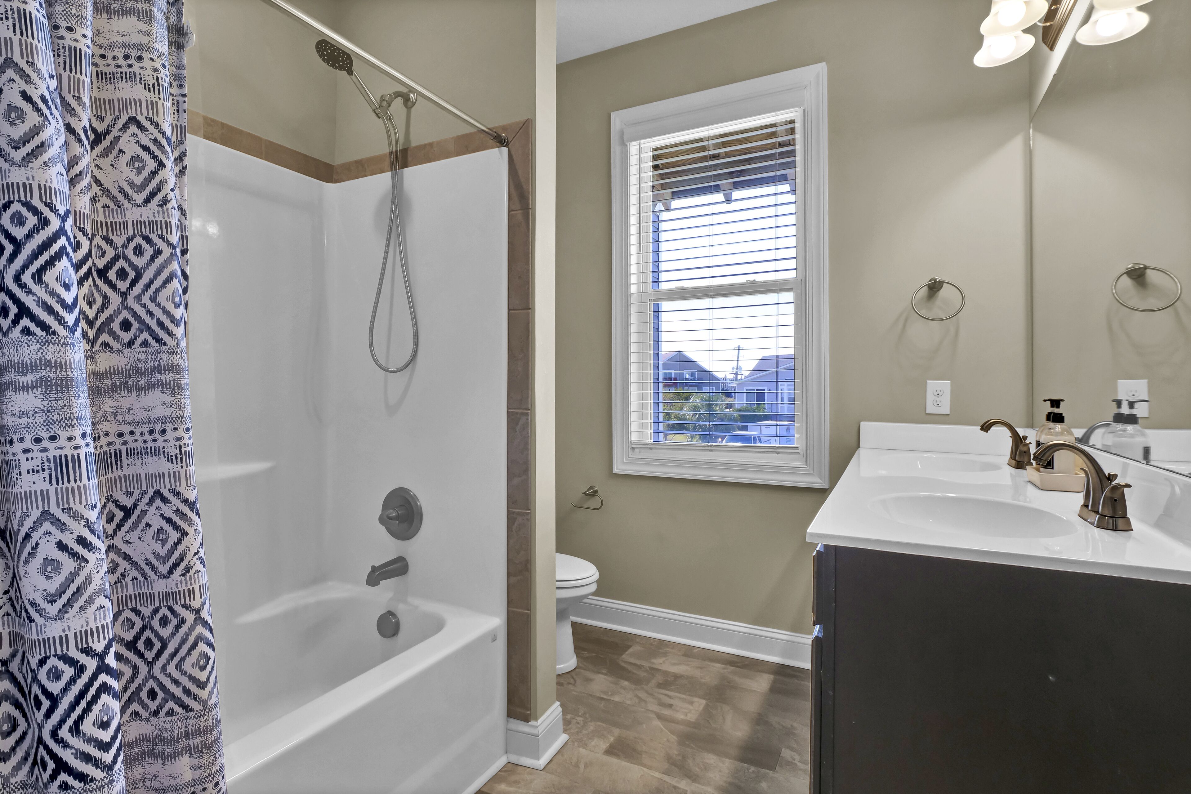 A bathroom with a bathtub, toilet, and a window with blinds.