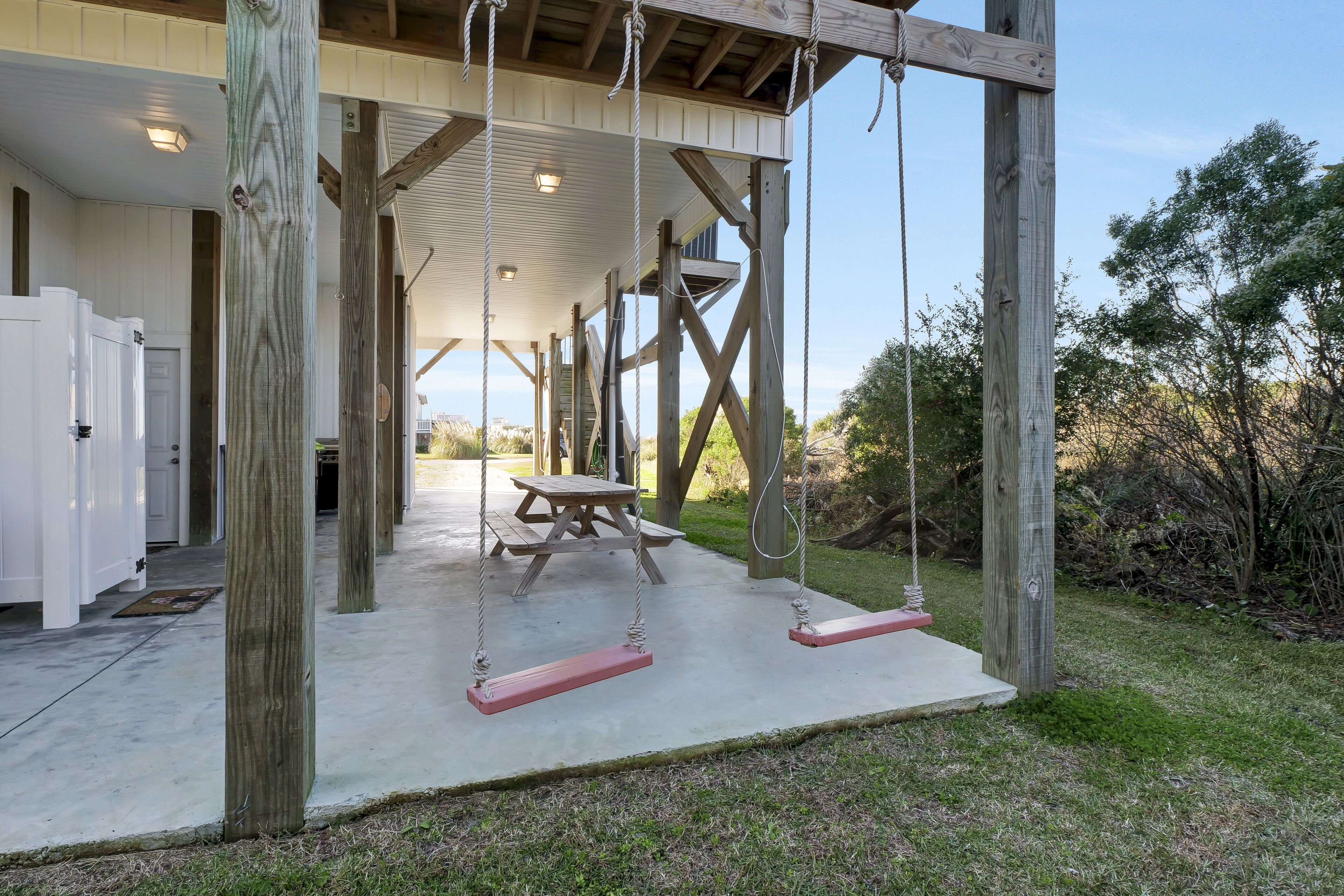 A wooden deck with swings, a picnic table, and a covered area with a door.