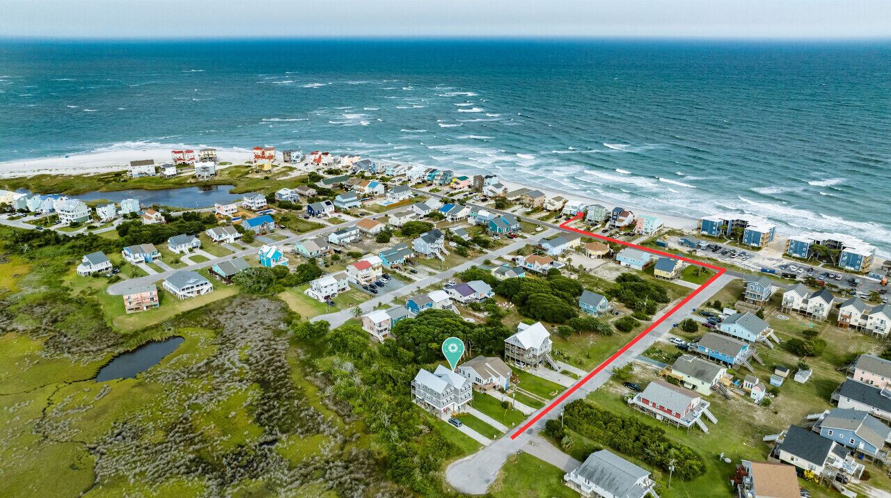 An aerial view of a coastal residential area with houses, a beach, and a marked path.