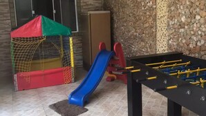 Un espace de jeux équipé d’un toboggan, d’un petit baby-foot et d’une structure de jeux en forme de filet.