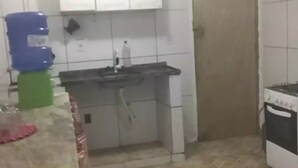 Une petite cuisine avec des meubles blancs, un évier, une cuisinière et un sol carrelé.