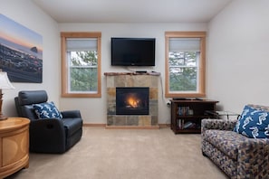 A living room with a fireplace, two windows, a television, a sofa, and a chair.