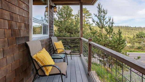 Une terrasse en bois avec deux chaises et des coussins jaunes, donnant sur une zone boisée.