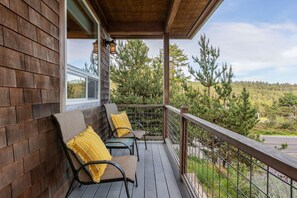 A wooden deck with two chairs and yellow cushions, overlooking a forested area.