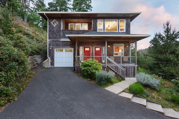 A two-story house with a garage, a red door, and a staircase leading to the entrance.