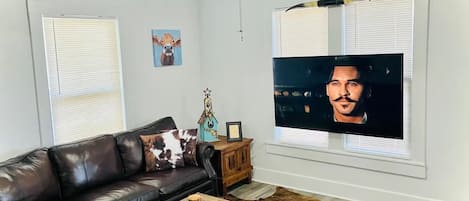 A living room with a leather sofa, a wooden coffee table, a ceiling fan, and a television on a wall.