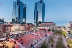 A city square with modern buildings, a central open area with seating, and a large illuminated structure.