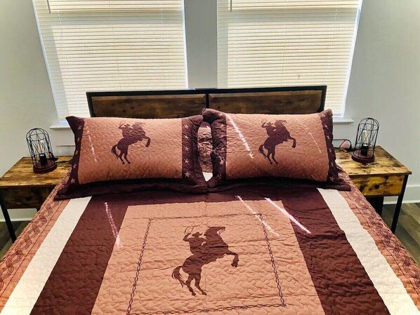 A bed with a quilted headboard, two nightstands, and a window with blinds.