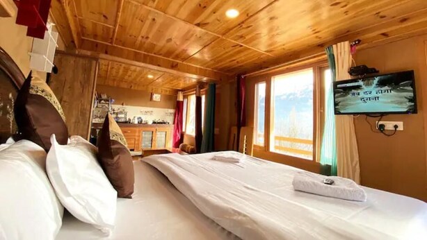 A wooden cabin room with two beds, a TV, and a kitchen in the background.