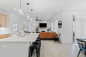 Une cuisine moderne dotée d’un îlot central, de tabourets de bar, de luminaires suspendus et d’un grand téléviseur placé au-dessus de l’îlot.