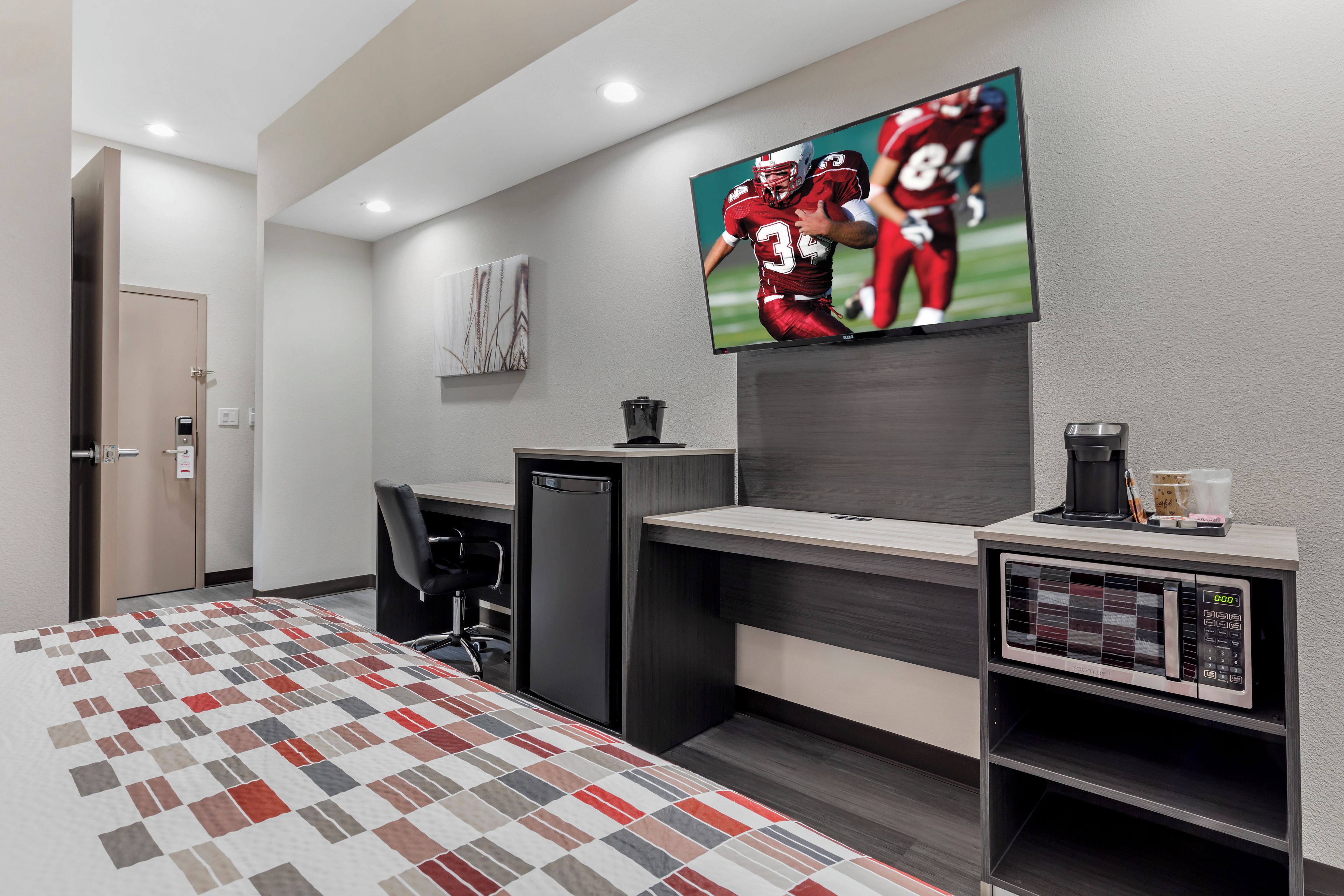 Una habitación de hotel con cama, escritorio, silla, televisor, cafetera y refrigerador.