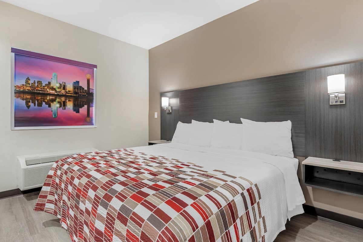 A hotel room with a large bed, a cityscape painting, a modern headboard, and a bedside table with a lamp.