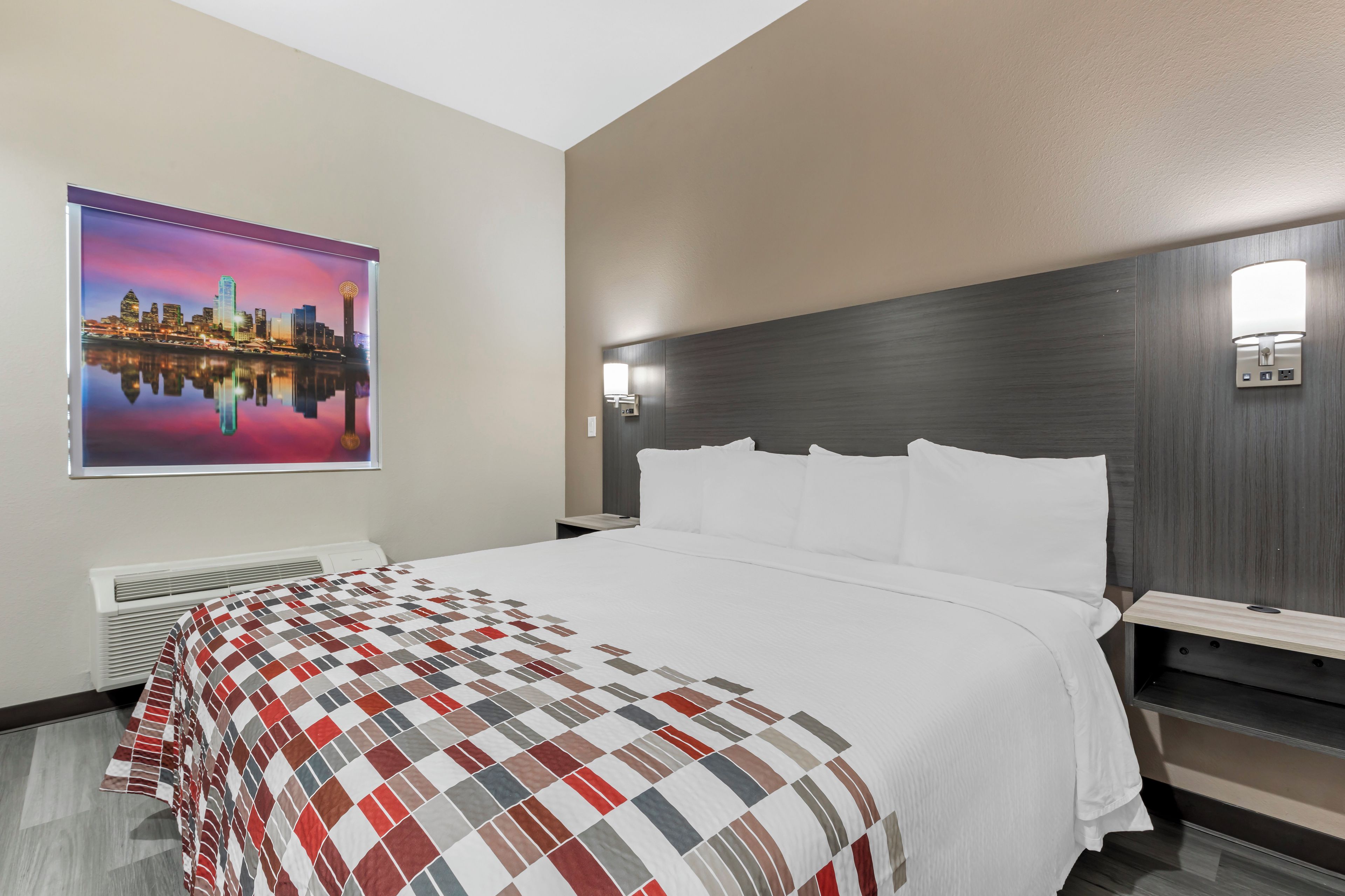 A hotel room with a large bed, a cityscape painting, a modern headboard, and a wall-mounted light fixture.