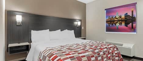 Una habitación de hotel con cama, mesita de noche, aire acondicionado de pared y un cuadro de paisaje urbano.