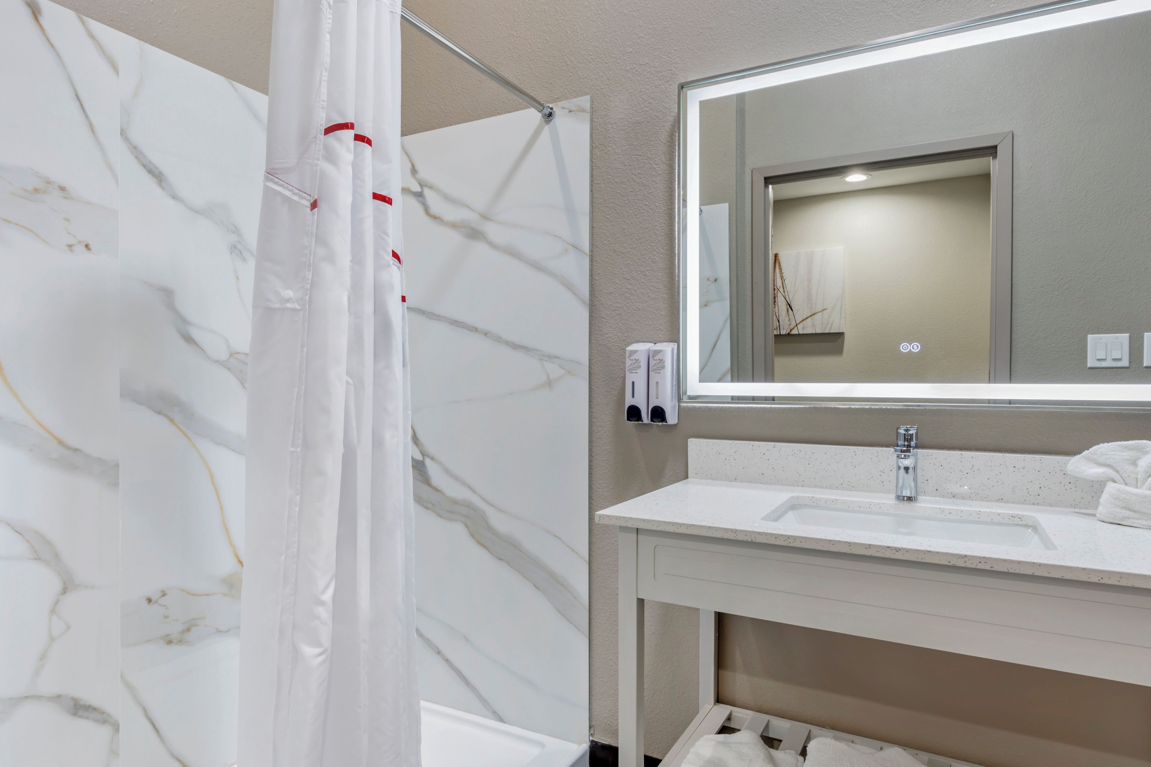 Un baño con pared de mármol, cortina de ducha, lavamanos, espejo y toalla.