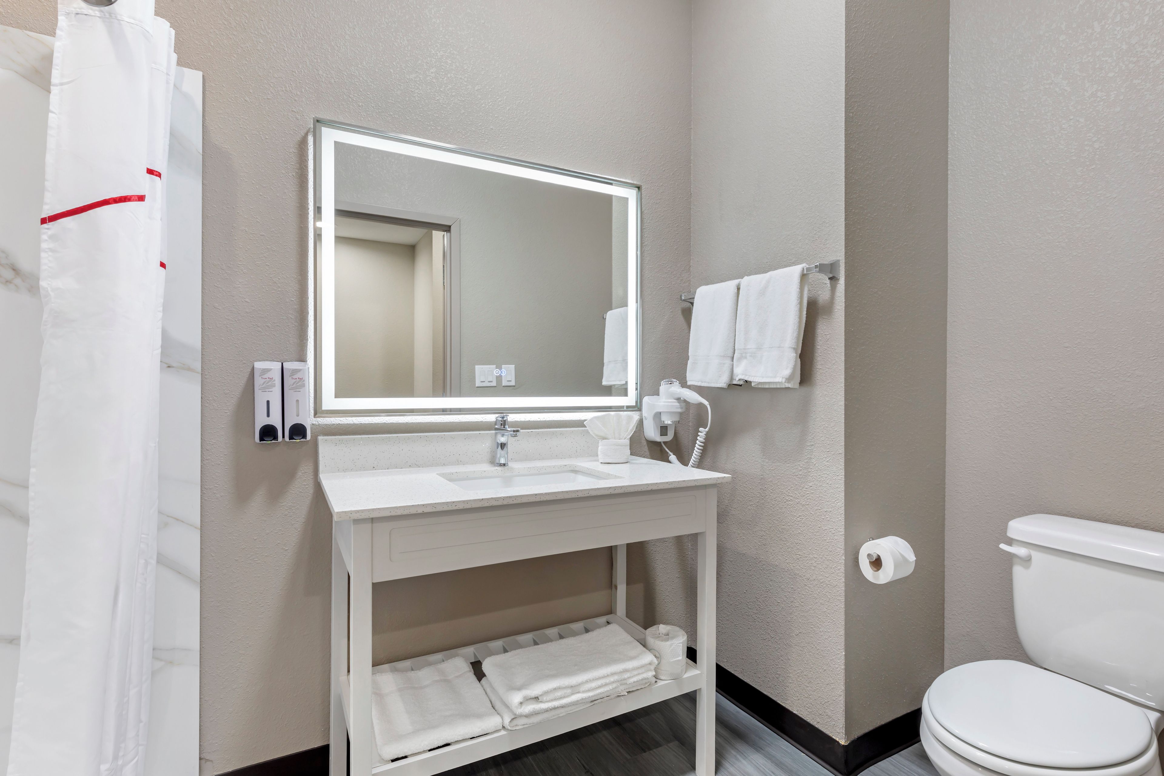 A bathroom with a white sink, mirror, and toilet. There are towels and a shower curtain.