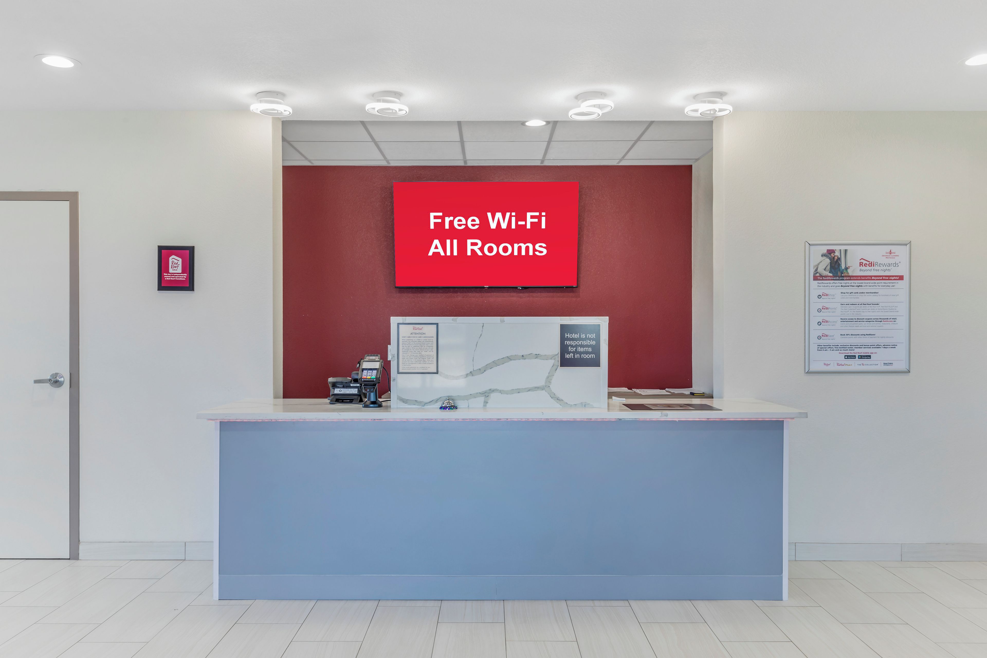 A reception desk with a red sign stating 'Free Wi-Fi All Rooms' and a digital display.