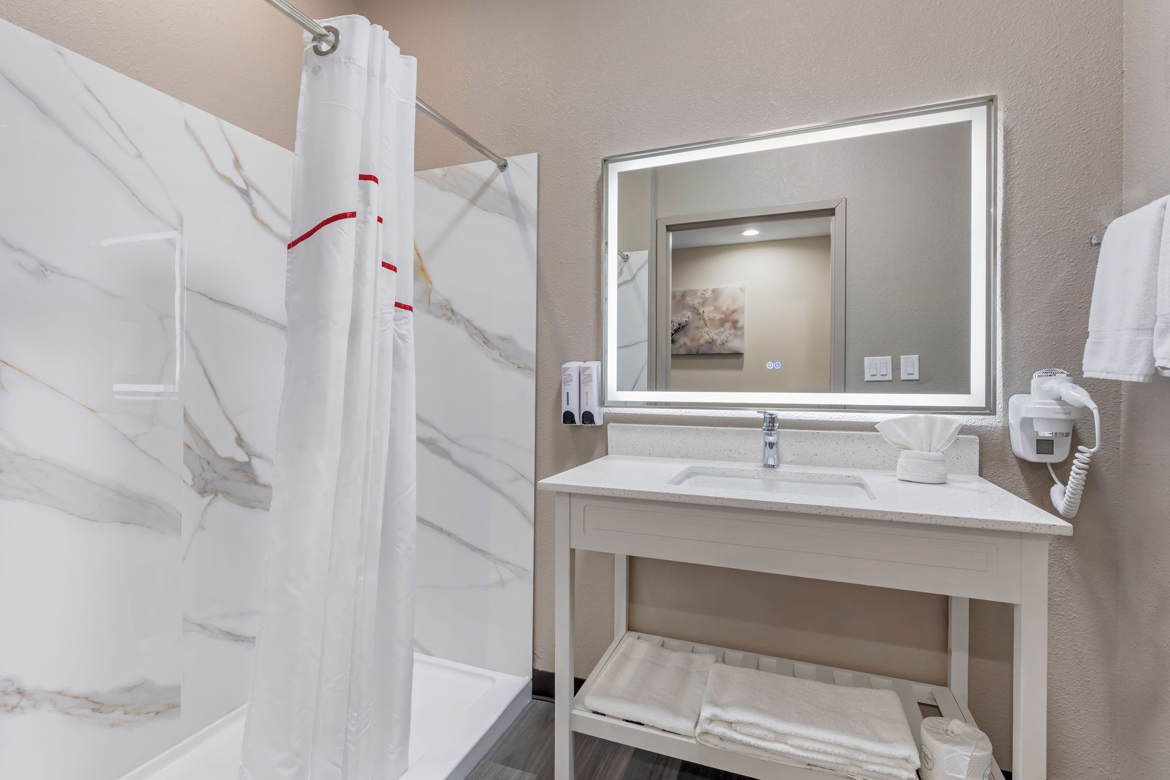 A bathroom with a marble shower wall, a white sink with a mirror, and a towel rack.