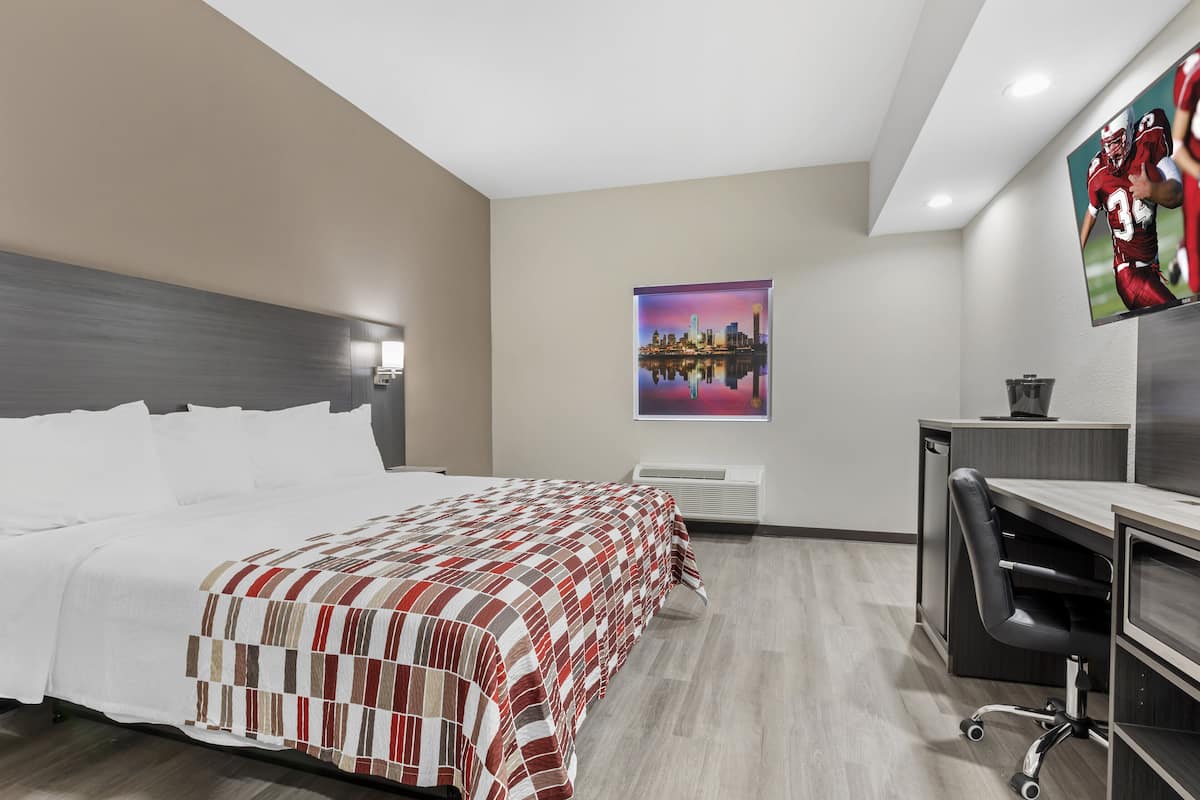 A hotel room with a bed, a desk, a chair, a TV, and a painting on the wall.