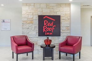 A Red Roof Inn sign on a stone wall with two red chairs and a vase on a small table. - Red Roof Inn Hutchins (Hutchins)