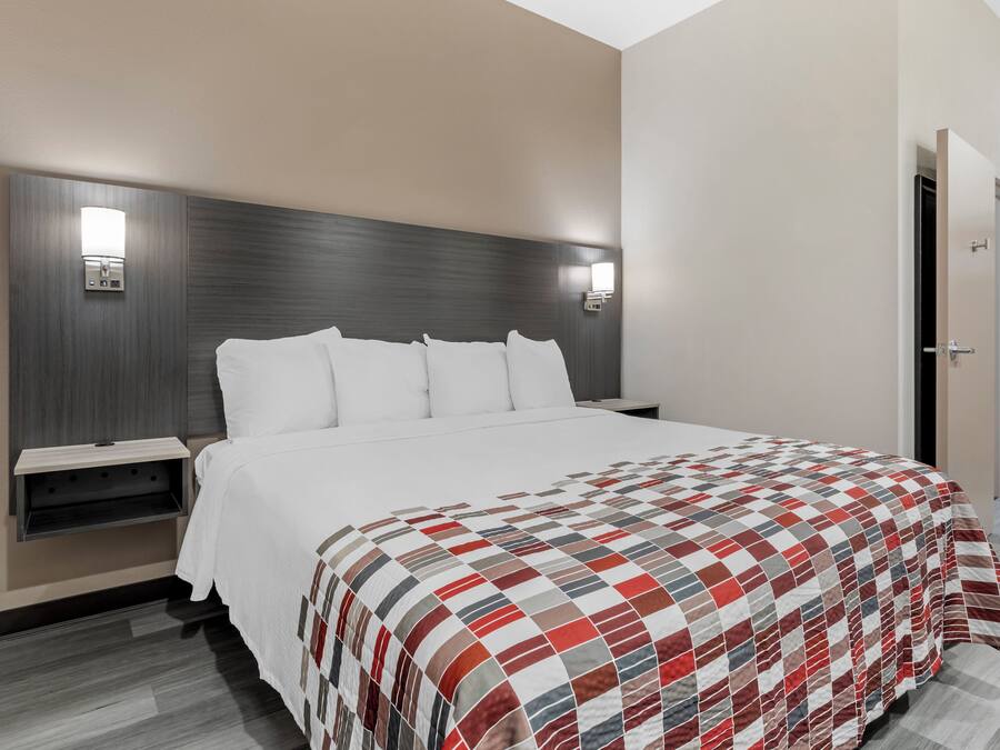 A hotel room with a large bed, a nightstand, a wall-mounted light, and a door.