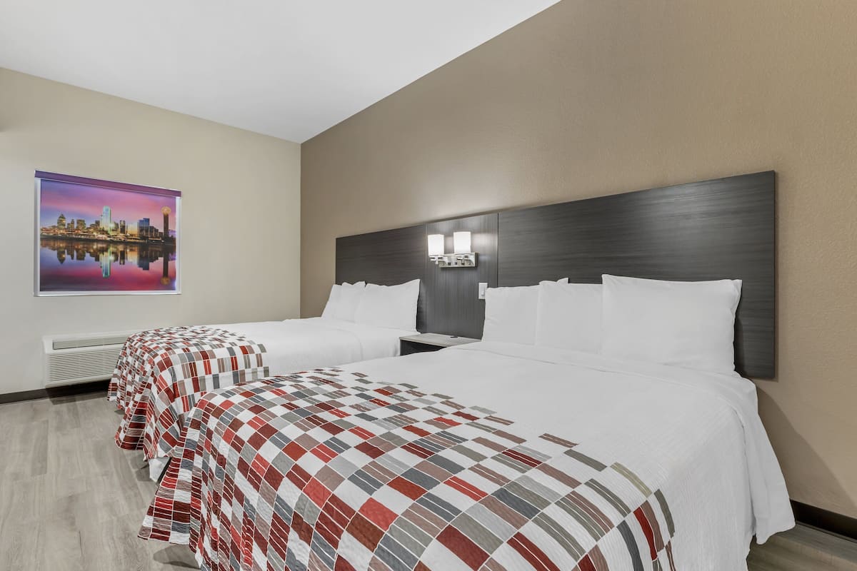 A hotel room with two beds, a cityscape painting, and a modern headboard with lighting.