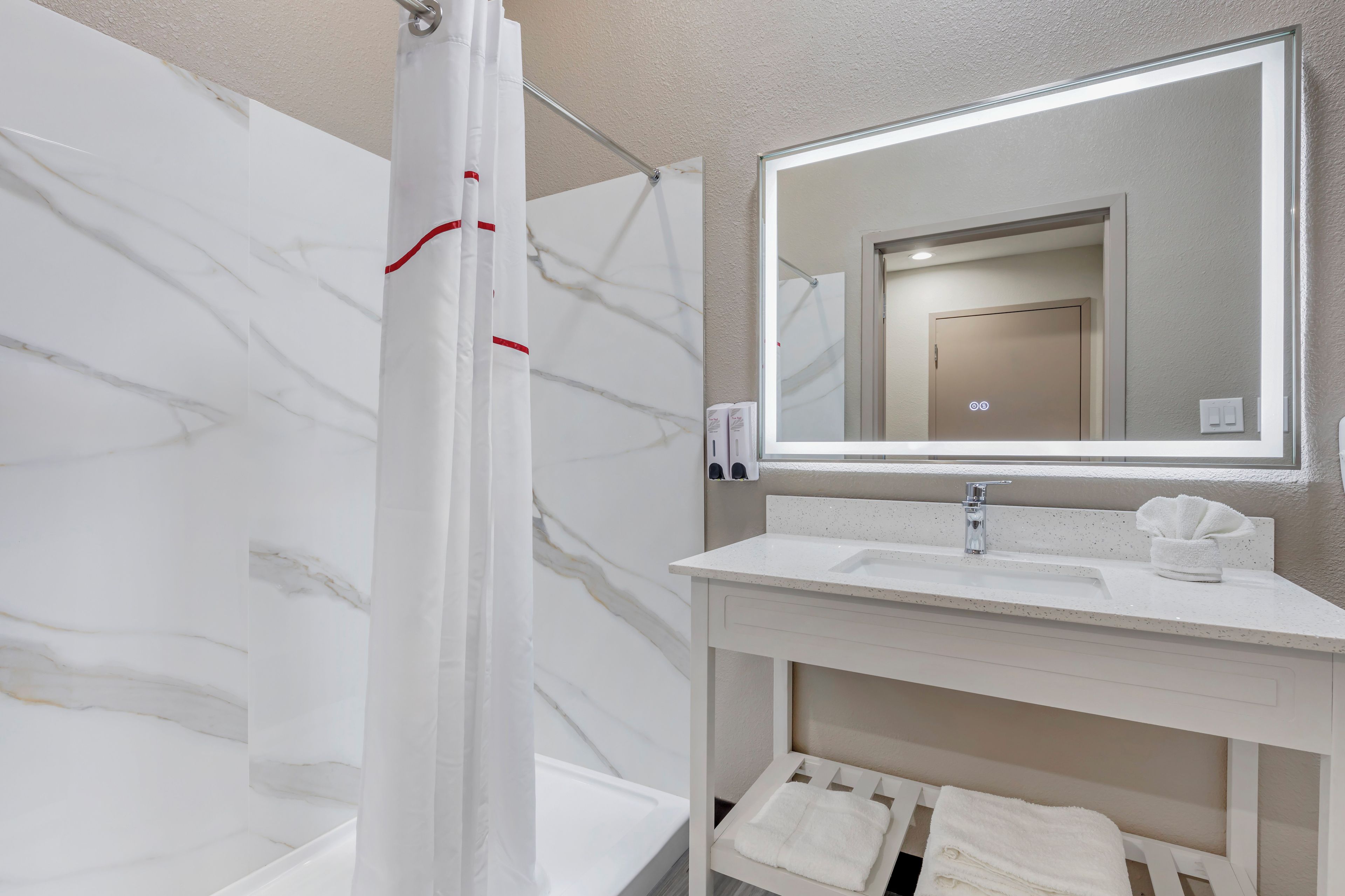 Un baño moderno con pared de mármol, cortina de ducha, lavabo con espejo y perchero para toallas.