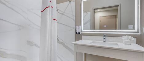 Un baño moderno con pared de mármol, cortina de ducha, lavabo con espejo y perchero para toallas.