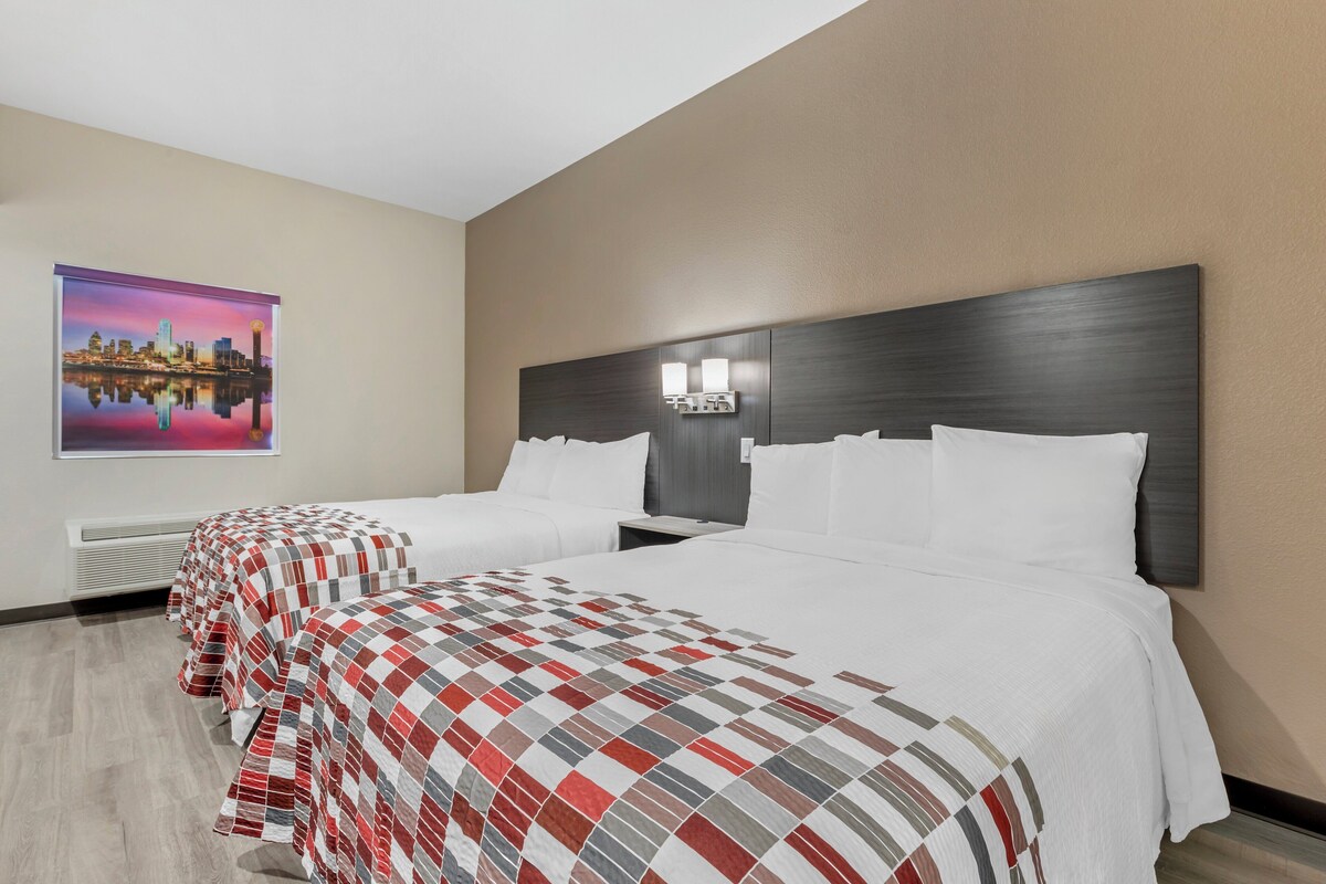 A hotel room with two beds, a cityscape painting, and a modern headboard with lighting.