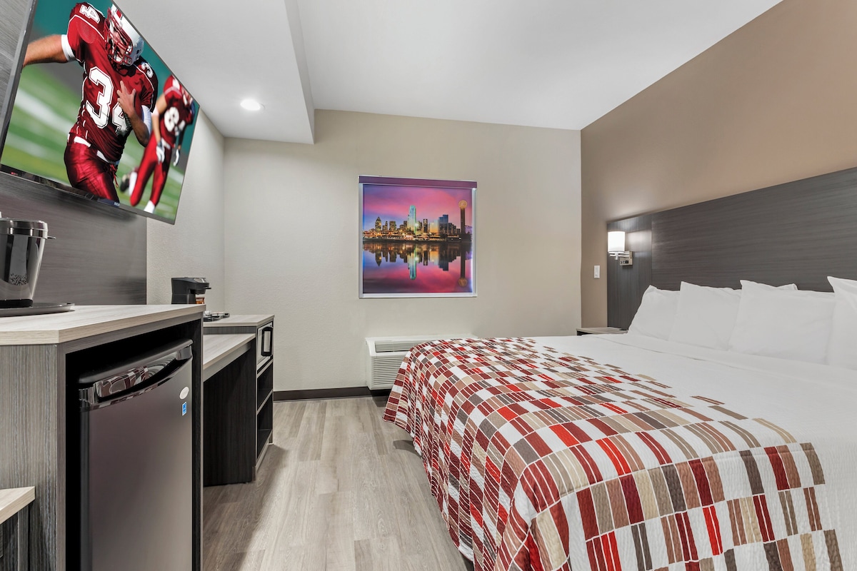 Hotelkamer met een bed, een bureau met een computer, een televisie en een stadsgezicht schilderij.