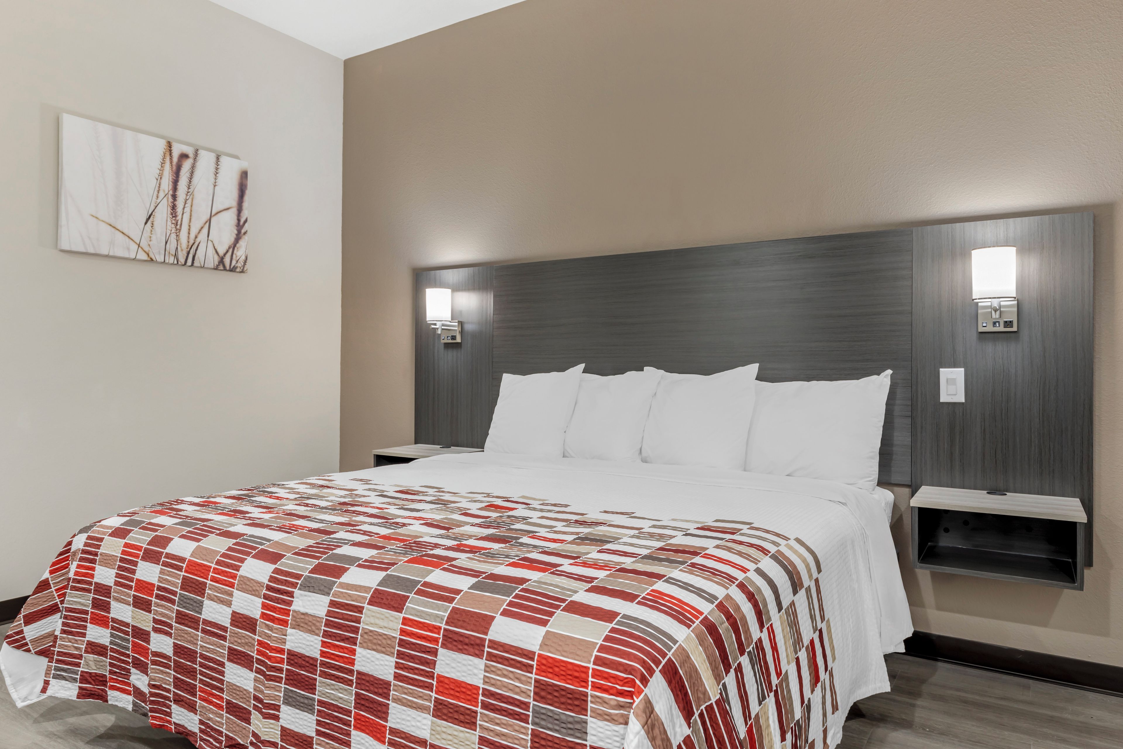 Ein Hotelzimmer mit einem großen Bett, einem mit Beleuchtung versehenen Kopfteil, einem Nachttisch und einem Wandbild.