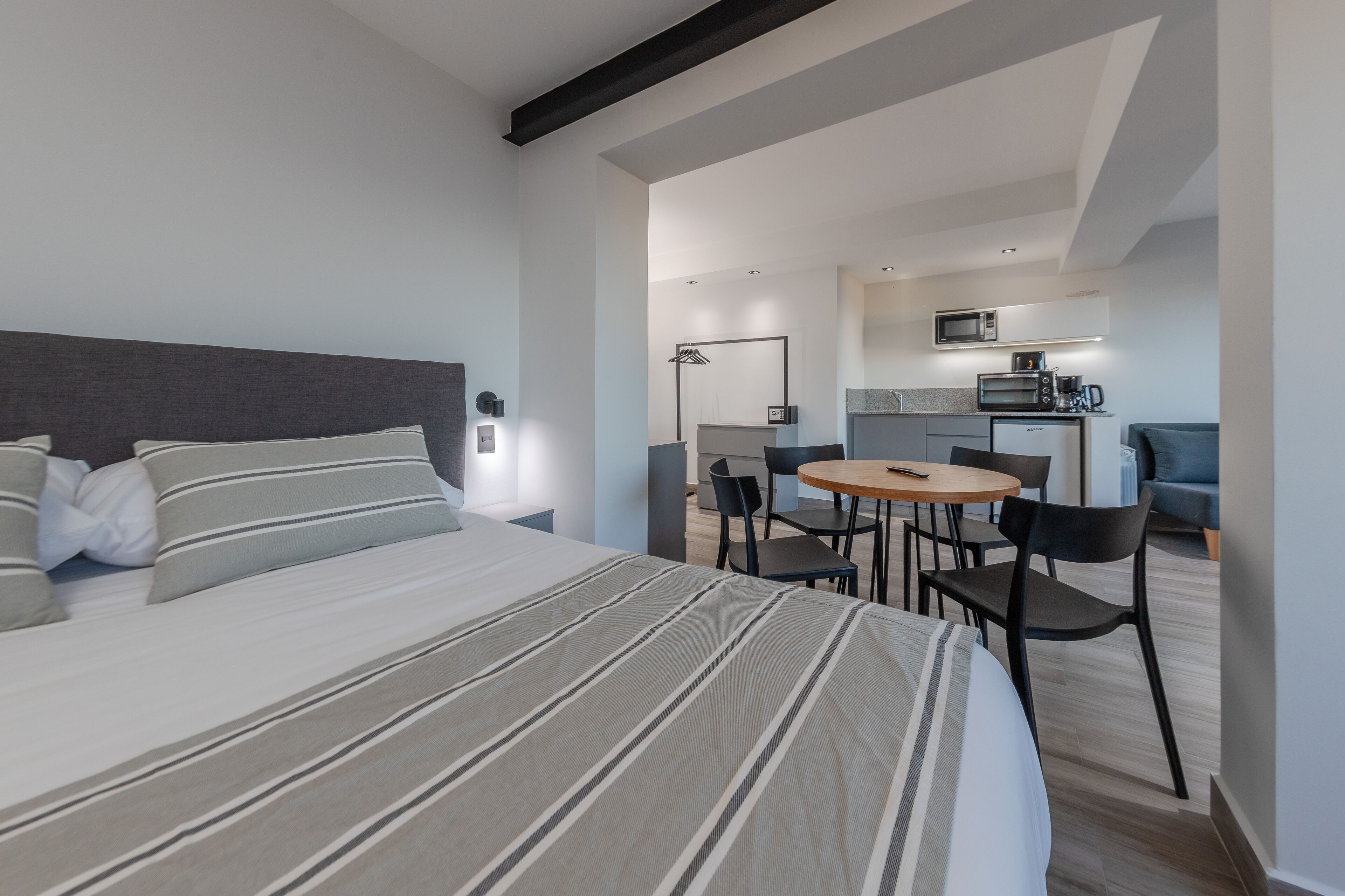 A modern hotel room with a large bed, a small dining area, and a kitchenette.