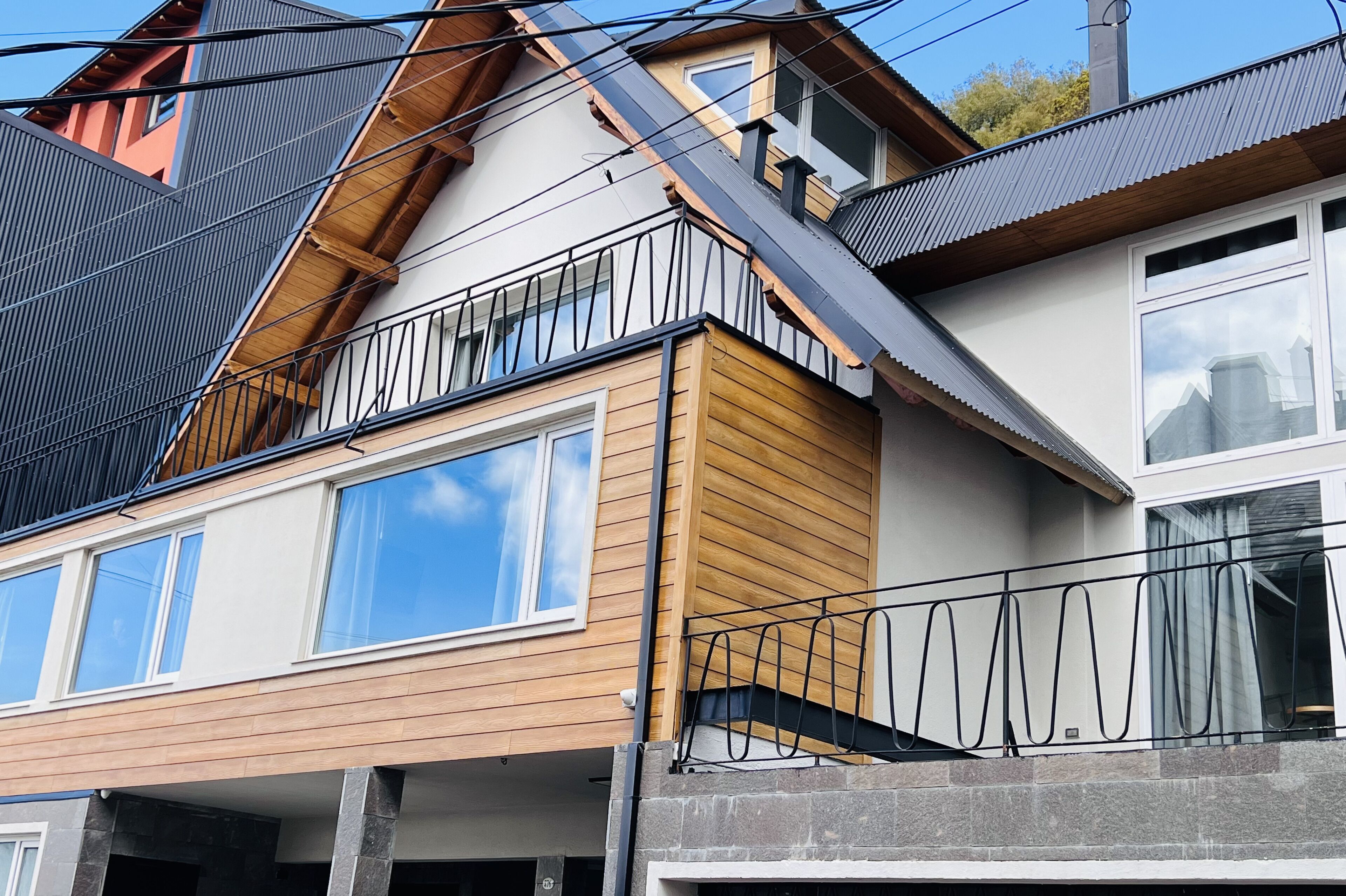 Una casa moderna de dos pisos con fachada de madera, ventanas grandes y un balcón con barandilla de metal.