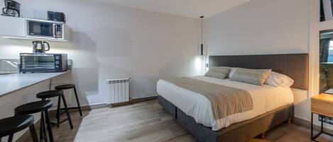 Un dormitorio moderno con cama, una kitchenette pequeña y una ventana.