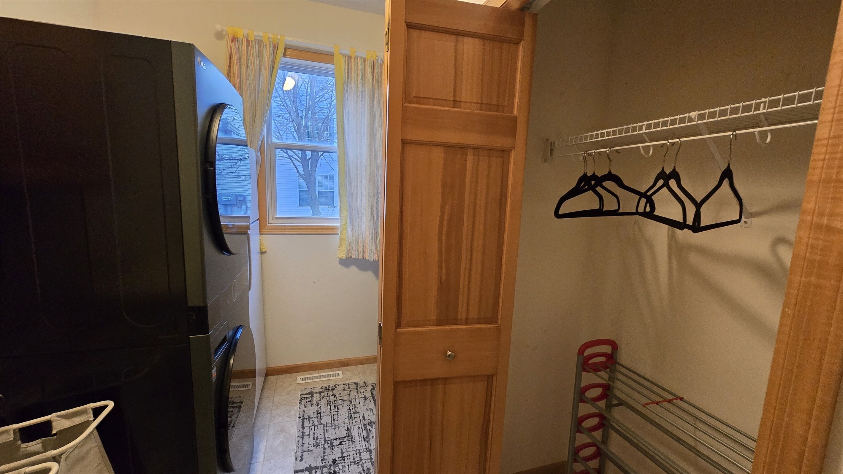 A room with a wooden door, a window with curtains, a wall-mounted clothes rack, and a tiled floor.