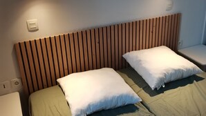 Huoneessa on kaksi sänkyä, joissa kummassakin on puinen pääty ja valkoiset tyynyt. Toisen sängyn vieressä on pieni pöytä ja tuoli.