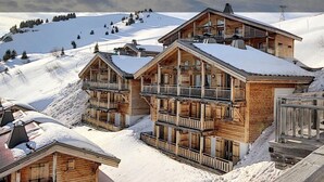 Un hôtel de style chalet en bois, doté de nombreux balcons et offrant une vue sur un paysage montagneux enneigé.