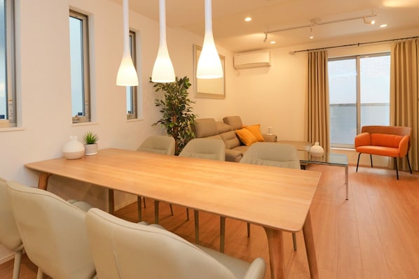 A modern living room with a wooden dining table, beige sofas, and a bright orange chair.