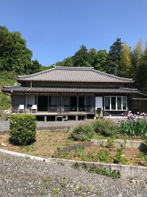 Ein traditionelles japanisches Gebäude mit einem Ziegeldach, großen Fenstern und einem Garten mit verschiedenen Pflanzen und Blumen.