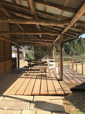 Eine überdachte Holzterrasse mit Picknicktisch und Stühlen, umgeben von einem Holzzaun und Bäumen.