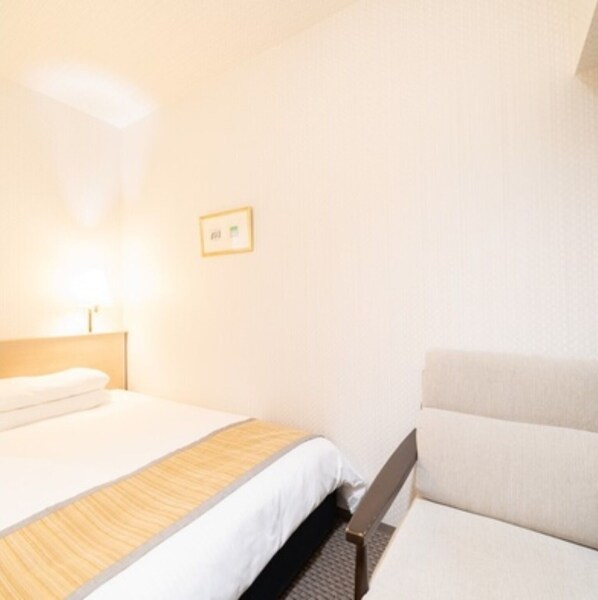 Habitación de hotel con cama, mesita de noche, una silla e imagen colgada en la pared.