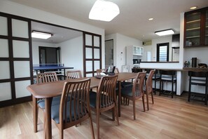 Un espace repas moderne avec une table et des chaises en bois, une cuisine en arrière-plan et une vue sur la ville à travers de grandes fenêtres.