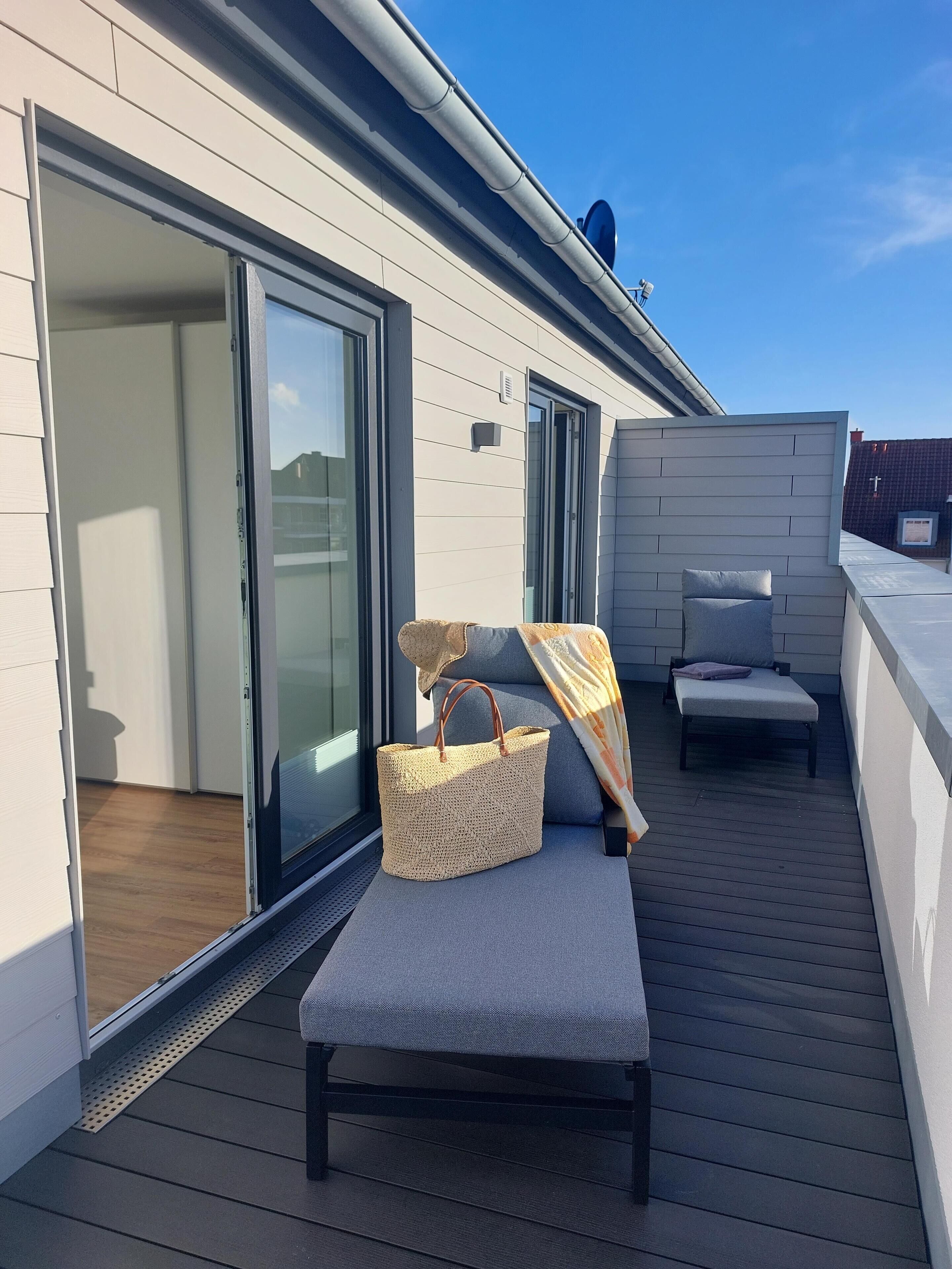 A balcony with a sliding glass door, a wicker basket, a cushioned bench, and a small table.