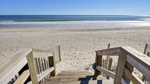 Una escalera de madera que baja a una playa arenosa con vistas despejadas al océano.