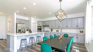Une cuisine moderne avec des meubles gris, un îlot central doté de tabourets et une table à manger avec des chaises de couleur turquoise.