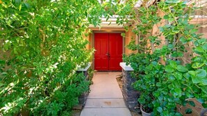 Un sentier menant à une porte rouge, entourée d’un feuillage verdoyant et luxuriant.